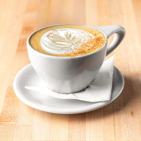 White cup of latte with art and cinnamon on a saucer and wooden table.