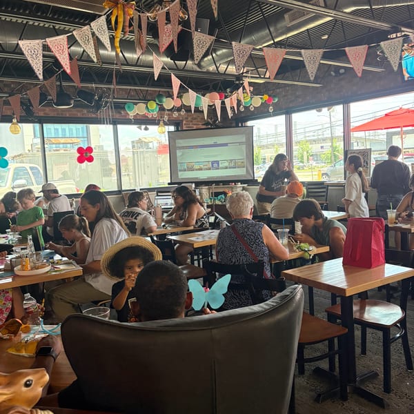 A lively restaurant interior with diverse patrons, festive banners, and a projected screen.