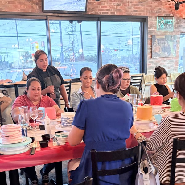 Women decorating colorful cakes at a long table in a brightly lit restaurant.
