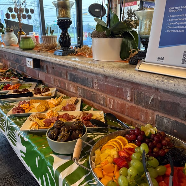 A buffet table with charcuterie boards, fruit, vegetables, and desserts, set against a brick wall.